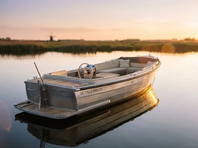 Moderne aluminium sloep op kalm water met gouden zonlicht reflecties in Nederlands polderlandschap