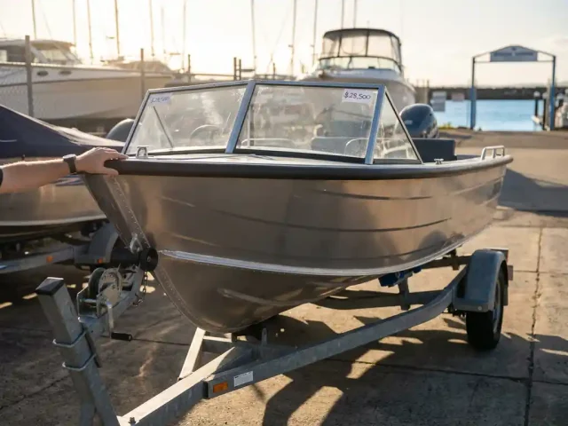 6-meter aluminium sloep te koop op trailer in jachthaven, koper inspecteert boot in zonnige verkoopwerf