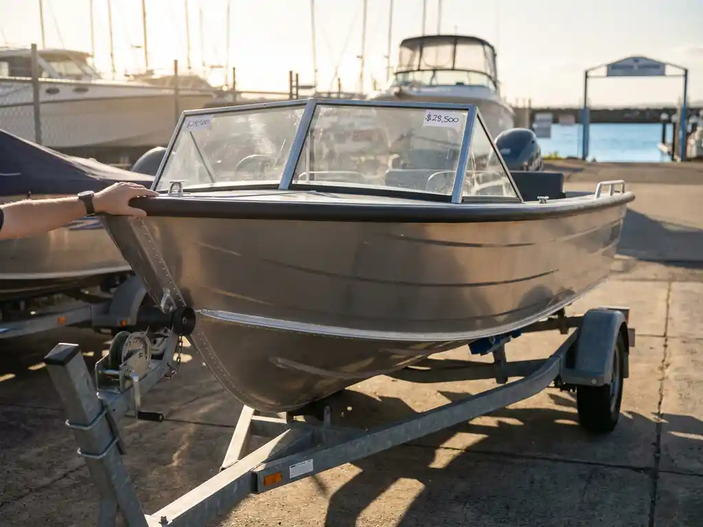 6-meter aluminium sloep te koop op trailer in jachthaven, koper inspecteert boot in zonnige verkoopwerf
