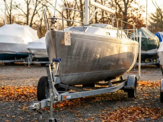 Aluminium zeilboot op trailer te koop in herfstjachthaven met gevallen bladeren en warme zonnestralen