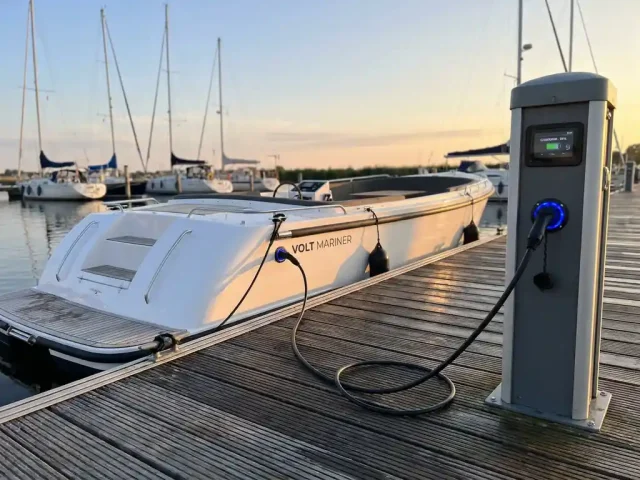 Witte elektrische sloep aan moderne steiger met oplaadkabel aangesloten op laadstation met blauwe LED-indicator