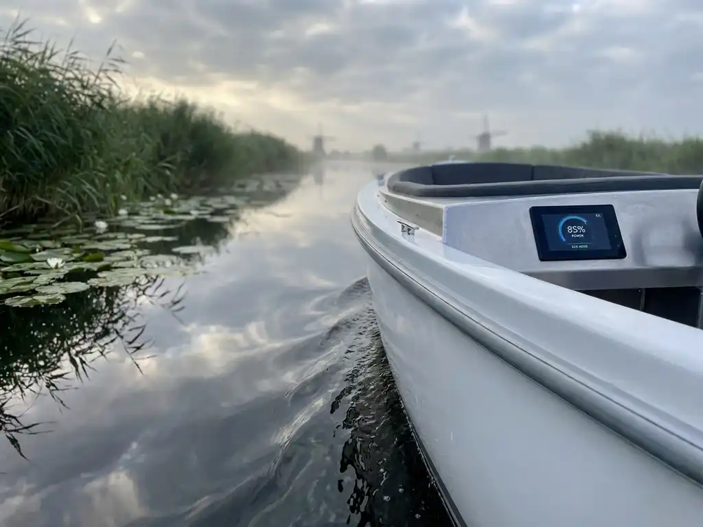Witte elektrische sloep vaart door kalm water tussen riet en waterlelies in Nederlands polderlandschap