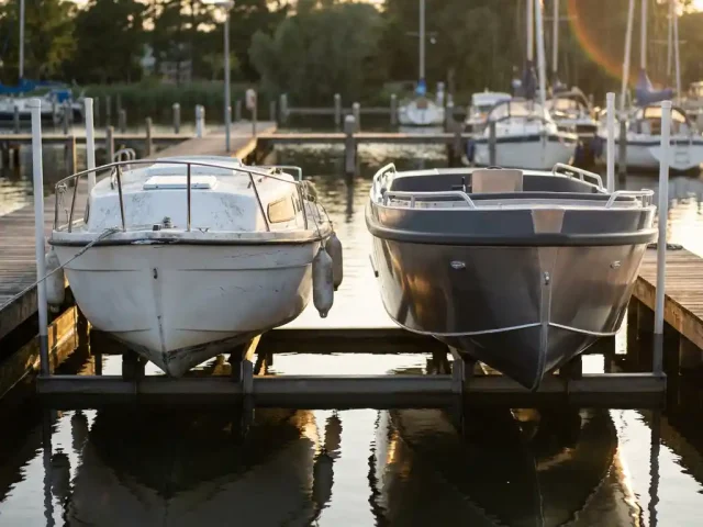 Twee sloepen op botenlift bij houten steiger: verweerde witte polyester boot naast nieuwe aluminium sloep in jachthaven