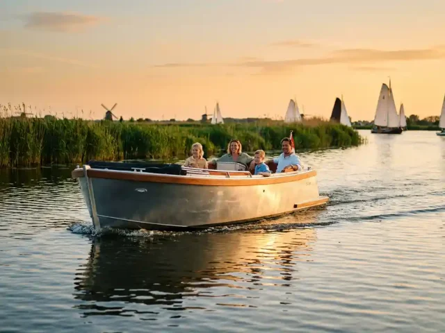 Moderne aluminium sloep met gezin vaart door kalme Nederlandse polderwaters tijdens gouden uur, rietoevers op achtergrond