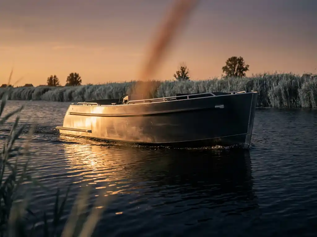 Aluminium tender sloep vaart over rustig Nederlands polderwater tijdens het gouden uur, rietkragen en lage horizon op de achtergrond.