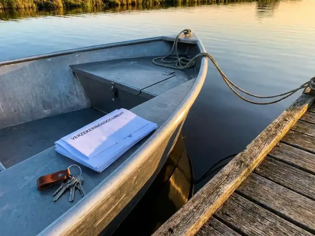 Aluminium tender afgemeerd aan houten steiger met verzekeringsdocument en sleutels op de romp, rustig polderwater in gouden middaglicht.