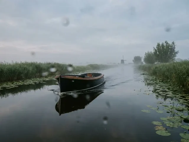 Elektrische sloep vaart door Nederlands polderwater bij ochtendmist, omringd door rietkragen en waterlelies.