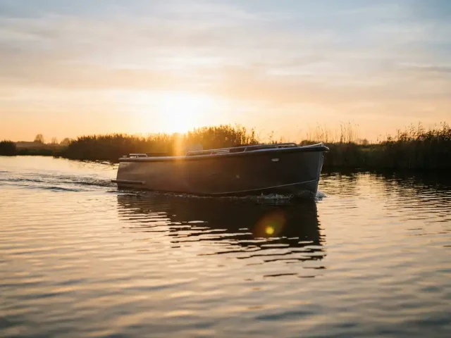 Antraciet aluminium tender boot vaart over rustig polderwaterwater tijdens gouden uur met rietkragen en weerspiegeling van amberkleurig licht.