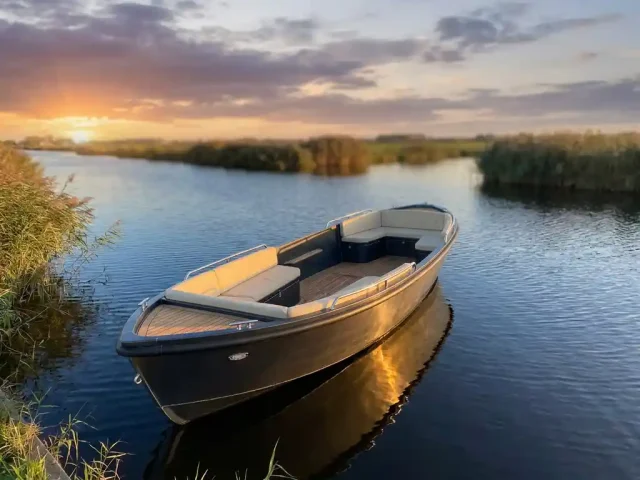 Aluminium tender op een rustige Nederlandse poldervaart, gouden uurlicht op de antraciet romp, crème kussens en teakhouten accenten zichtbaar.