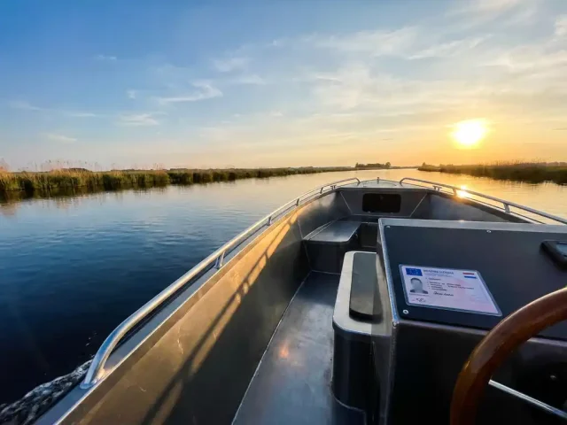 Antracietgrijze aluminium tender op rustig Nederlands polderwater met vaarbewijs op de console, gouden middaglicht.